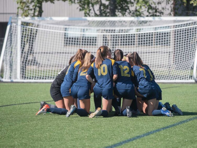 Kneeling group huddle of girls on soccer field.