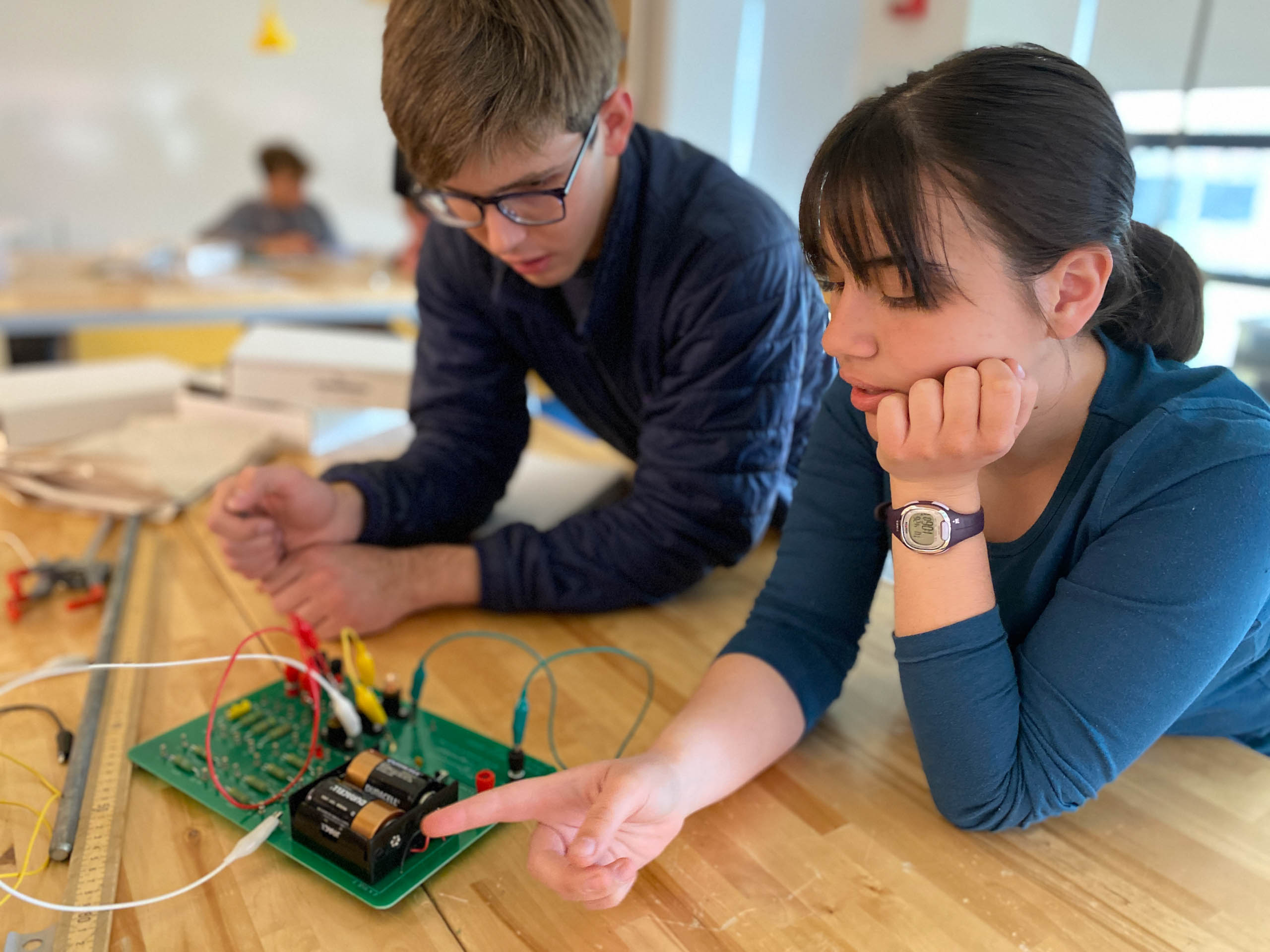 two teens working on circuit board in class.
