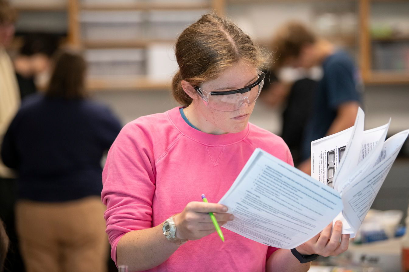 student reading notes in safety glasses.