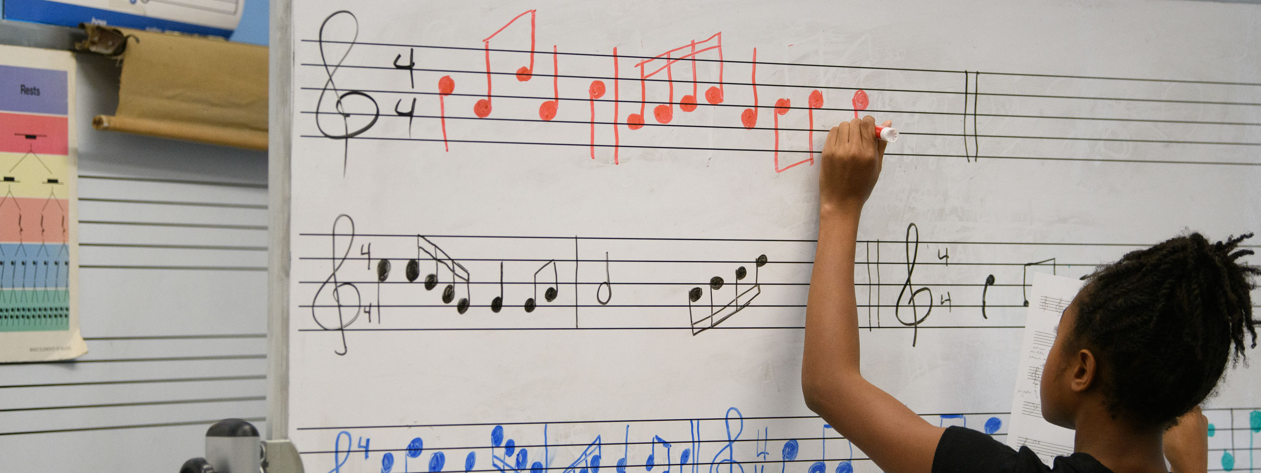student writing notes on sheet music whiteboard.