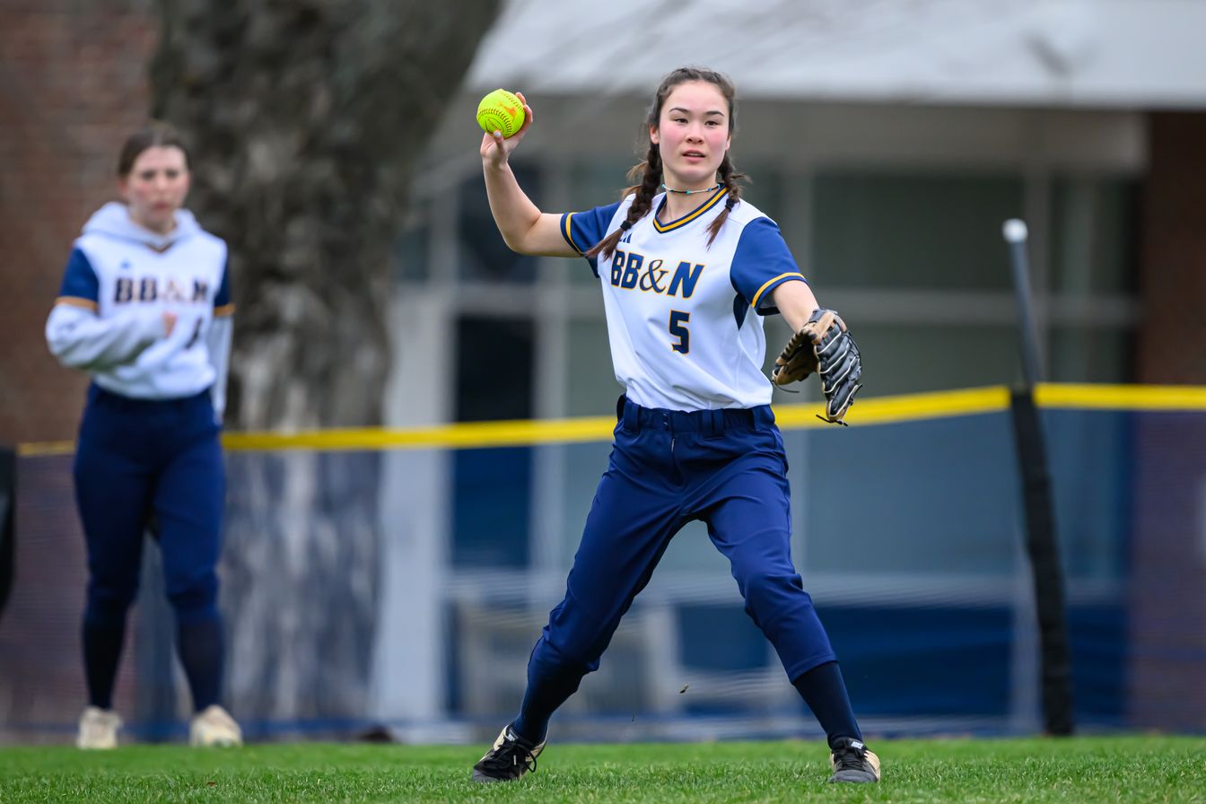 A girl in a softball uniform throwing a ball.