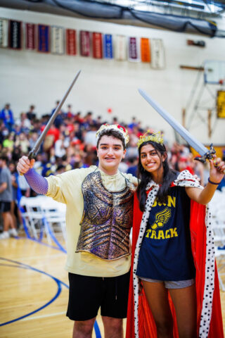 two students lifting swords in costume in gym.