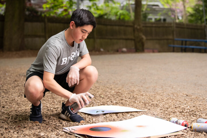 student spraying art outside.