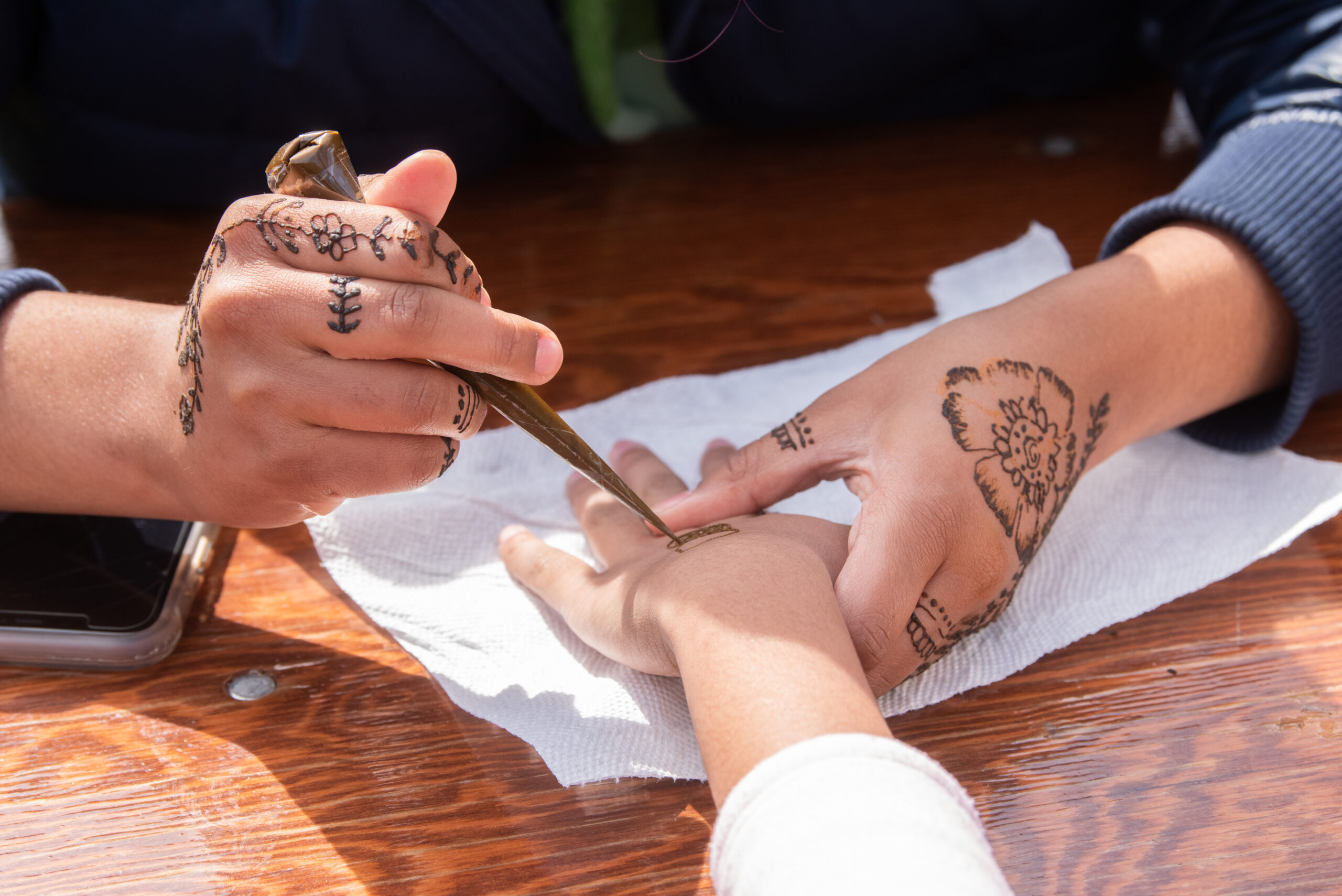 A person is applying henna designs on another person's hand, both of which have henna patterns.