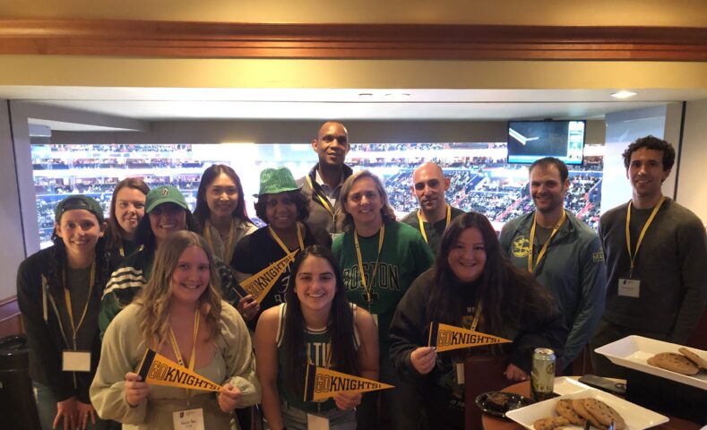 A group of people wearing green and yellow hold up "Go Knights" pennants in a sports arena suite.