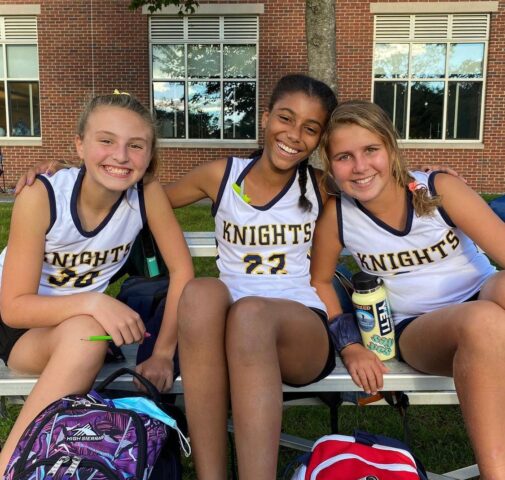 Three girls sitting on a bench with backpacks.