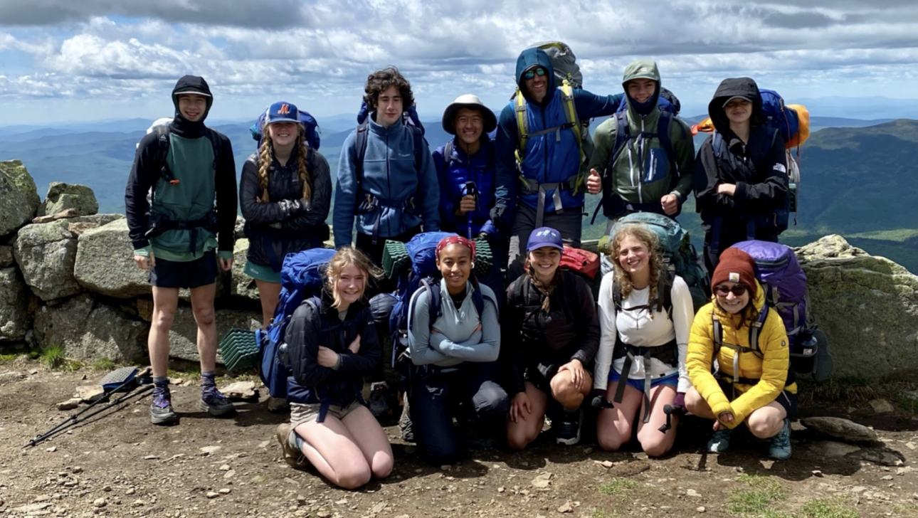 A group of people dressed in hiking gear posing for a photo on a rocky mountain trail with a scenic landscape in the background.