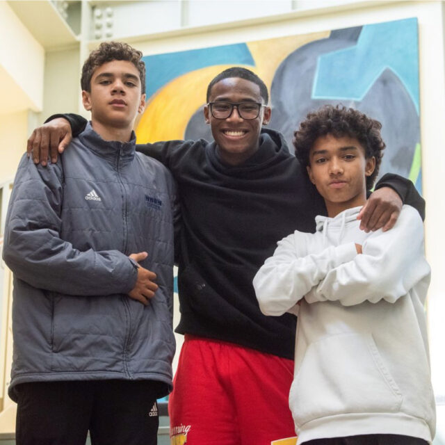 three boys standing and smiling.