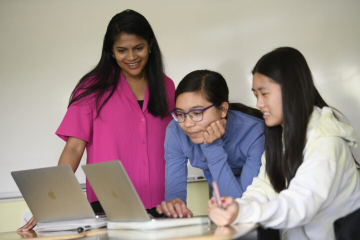 Three people engage in a discussion while looking at laptops.