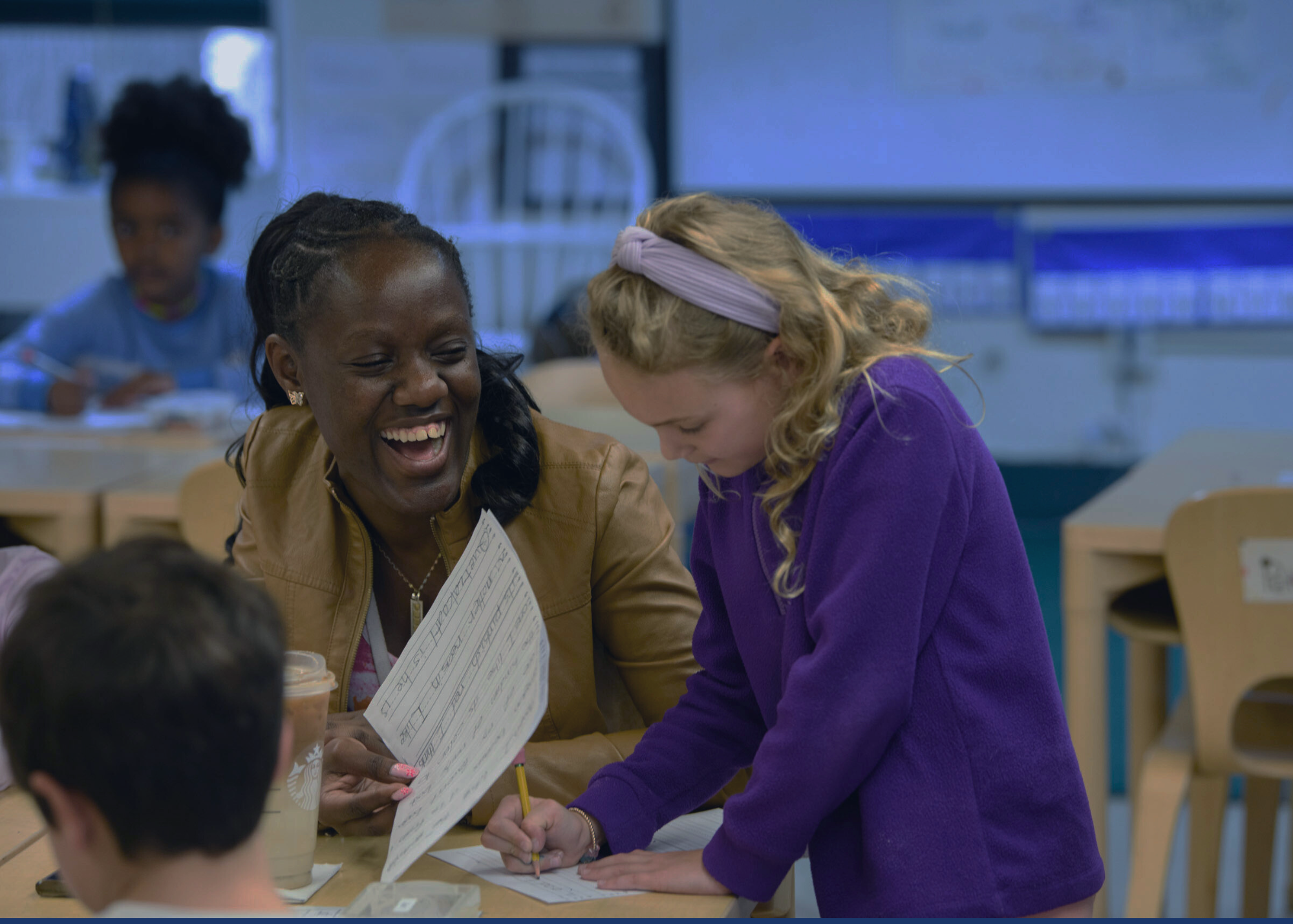 A woman and a young girl are smiling and interacting at a desk filled with papers.