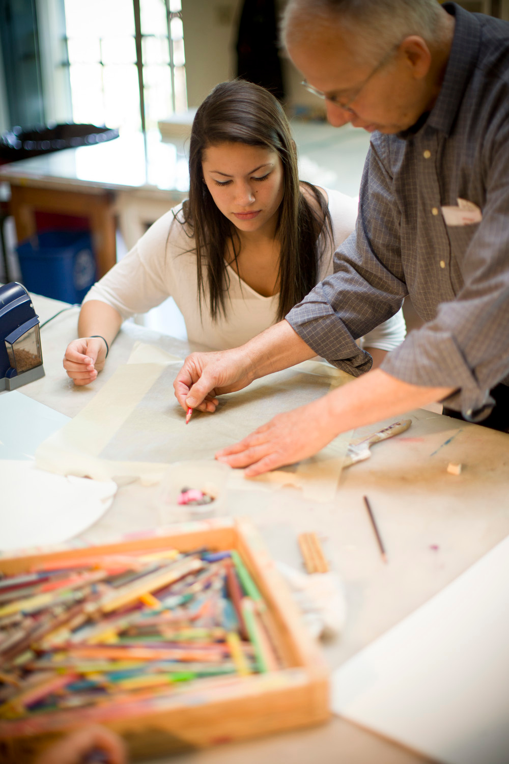 An older man and a young woman are working together on an art project at a table.