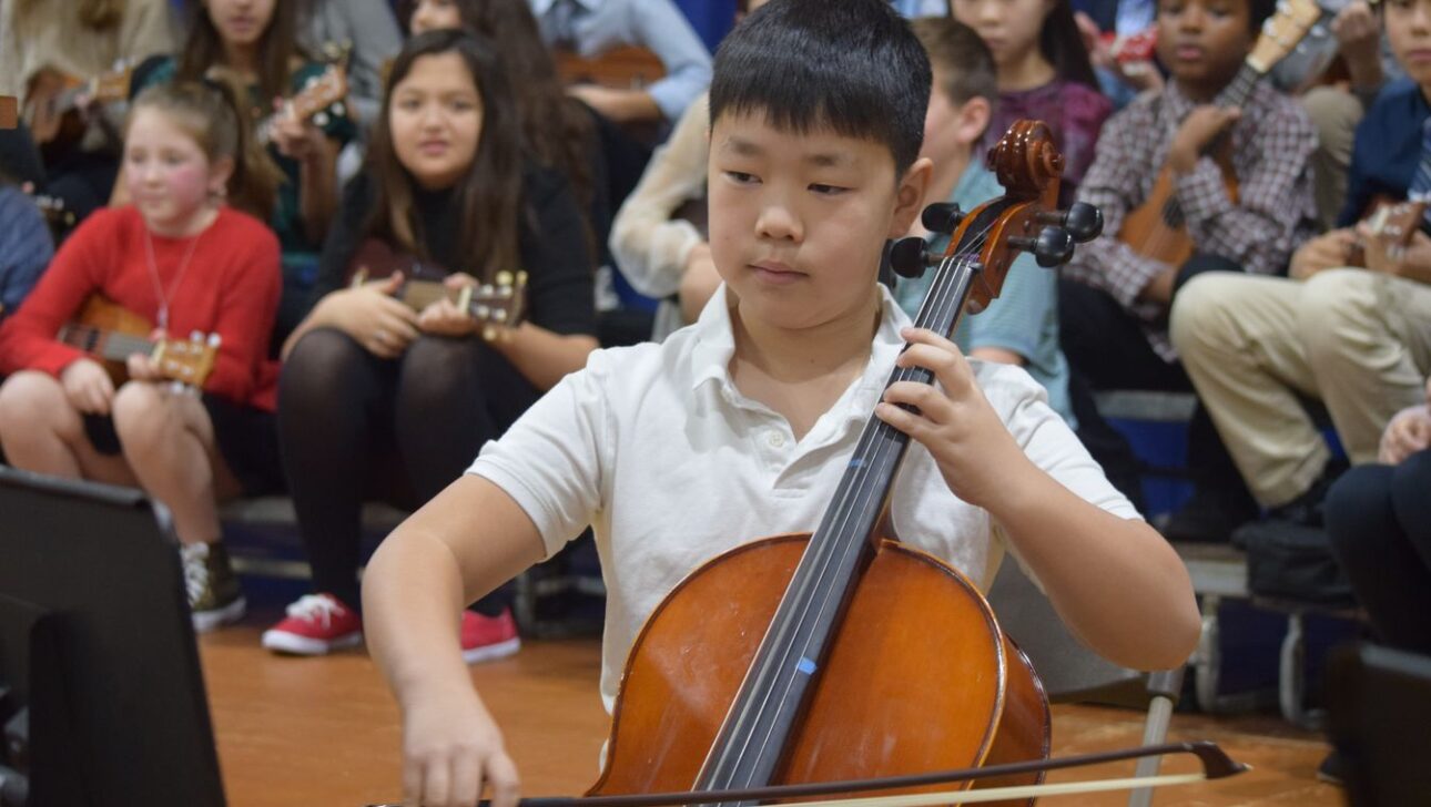 A young boy playing a cello in front of an audience.