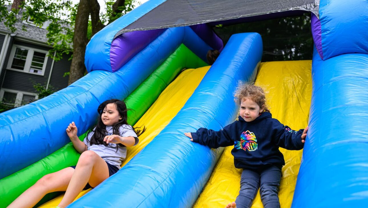 Two children slide down an inflatable slide; one is on the left with a relaxed position, and the other on the right appears focused.