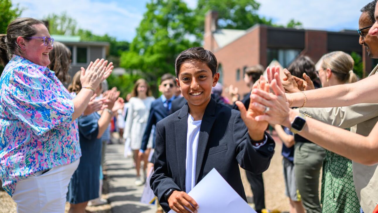 A young person in a suit walks down a path, high-fiving adults lined on either side.