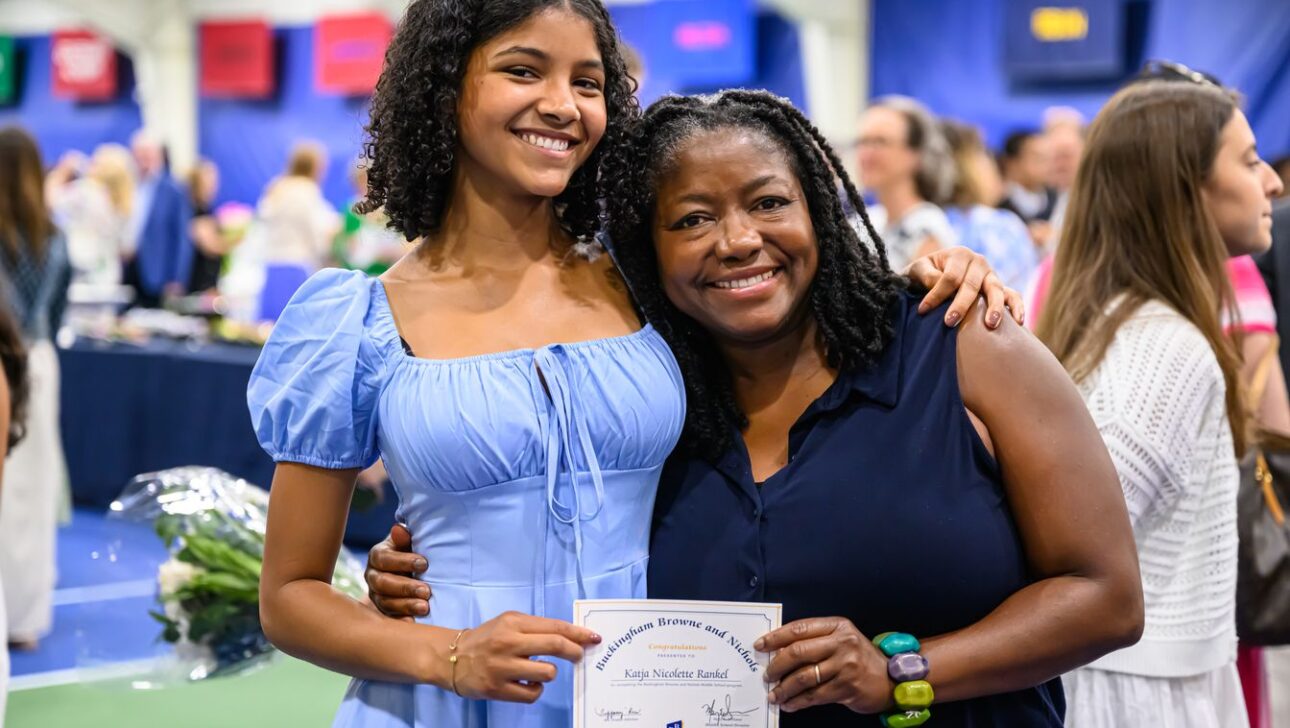 Two women smiling at a graduation ceremony; one holds a certificate.