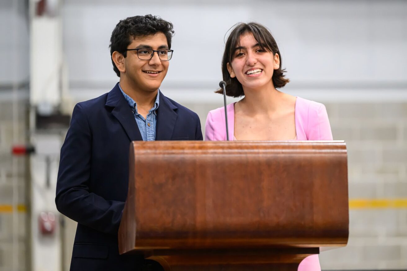 Two people standing behind a wooden podium, smiling.