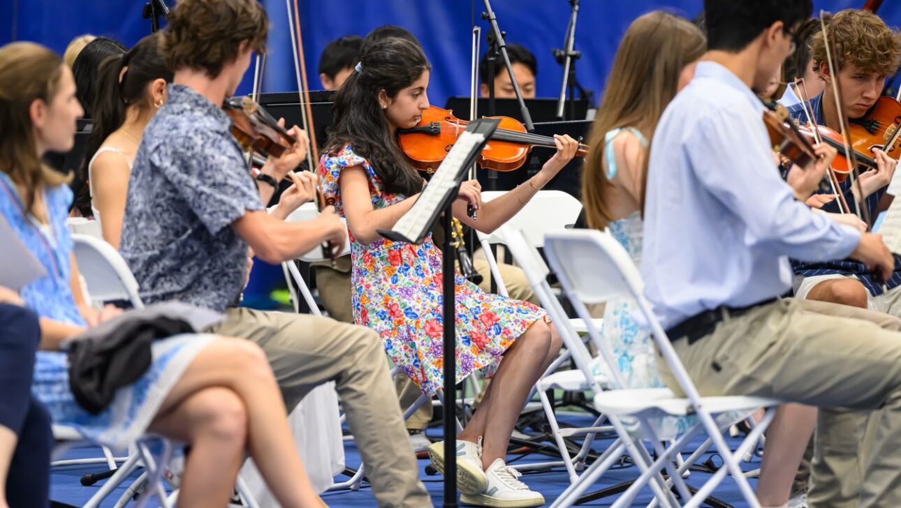 A group of young musicians sit in chairs and play violins during a performance.