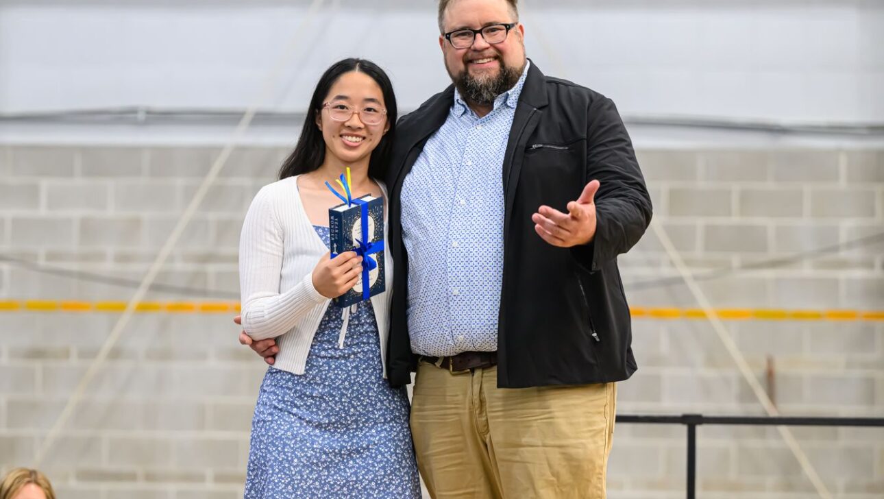 A woman in a blue dress holds a trophy while standing next to a man in a black jacket.