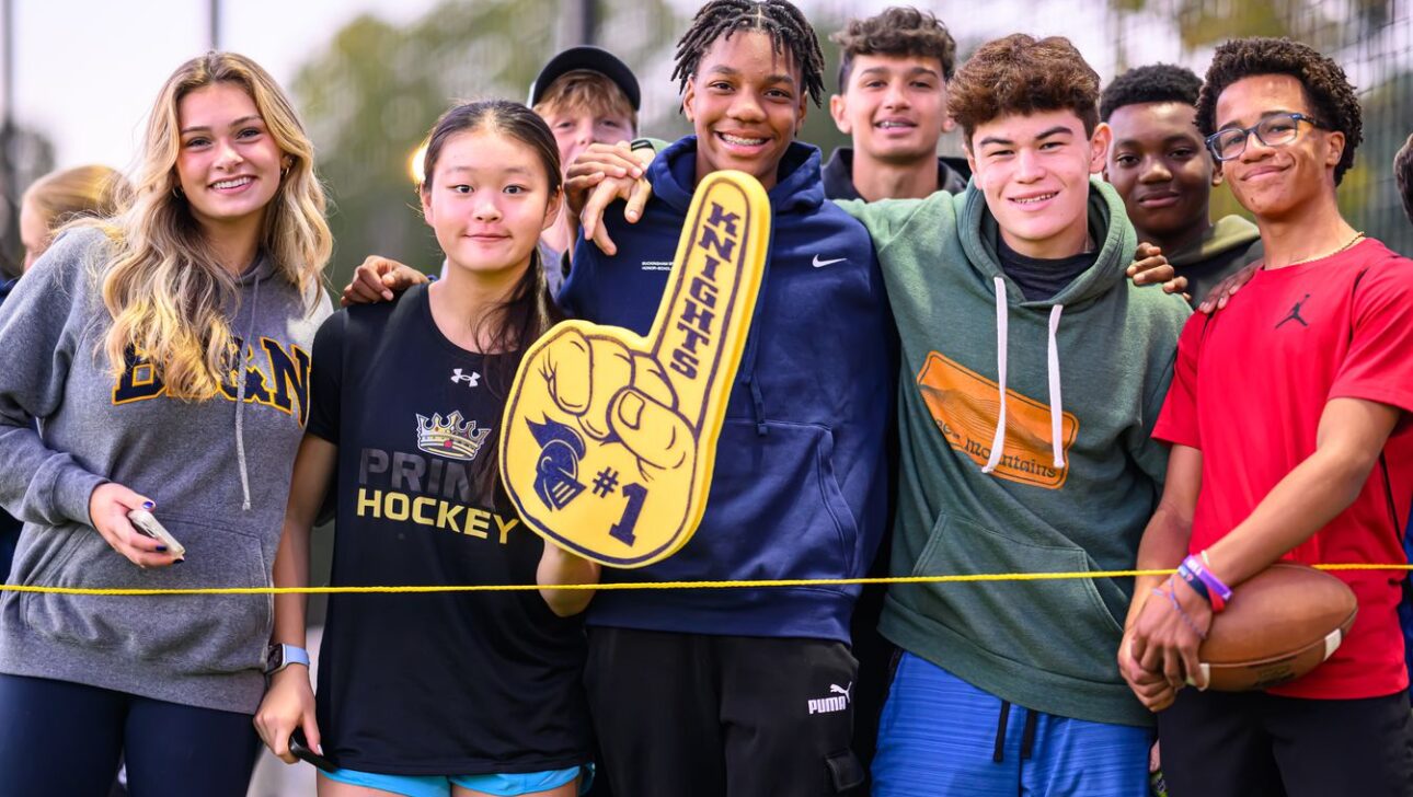 Group of diverse young people smiling at a sports event, with one holding a foam finger that says "Knights #1.