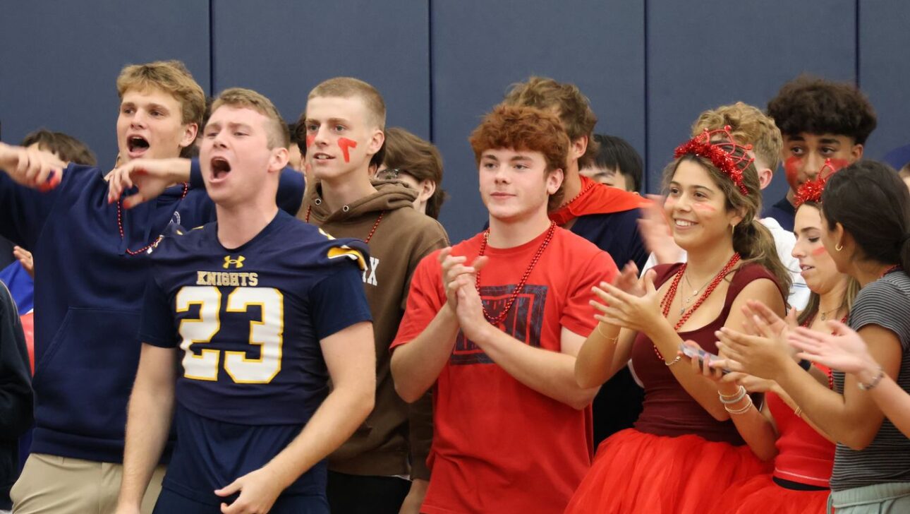 A group of students cheering enthusiastically, one wearing a sports jersey with the number 23, others in casual and red-themed outfits.