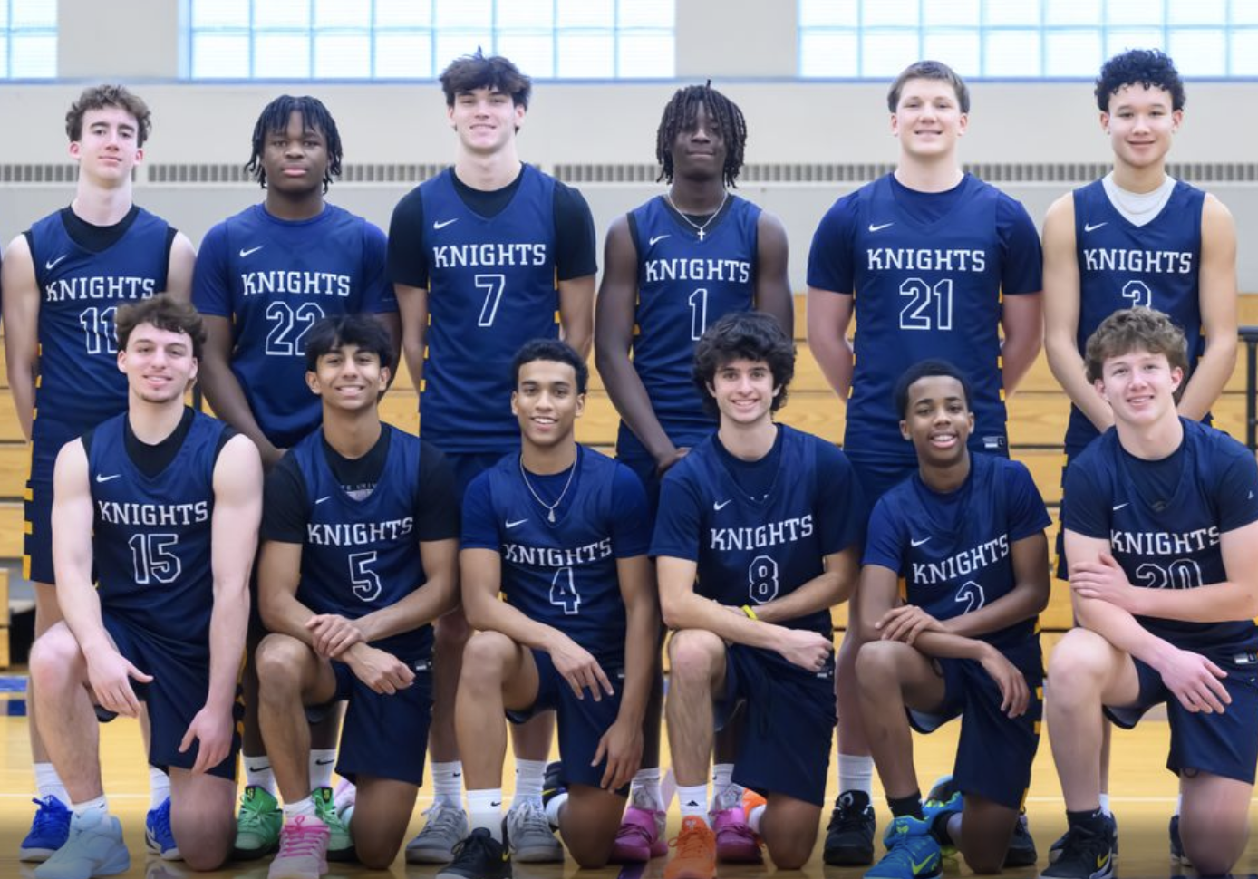 A boys’ basketball team wearing navy blue “Knights” uniforms poses together in a gymnasium, with players standing and kneeling in two rows.